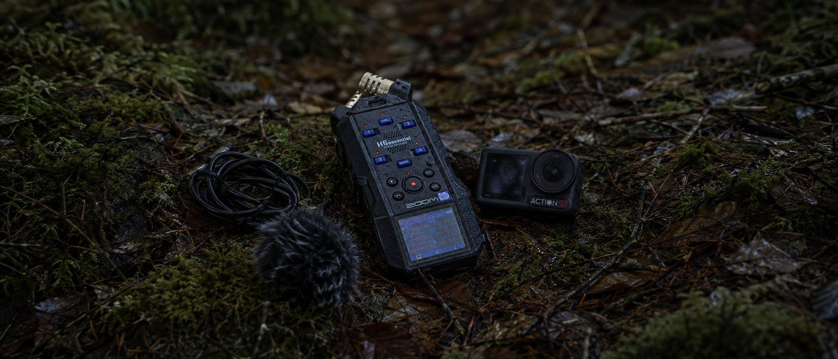 The recorder, action camera, a coiled cable and a fur windscreen resting on damp moss and leaf litter on a forest floor